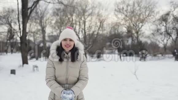 布吕内特的头发是年轻女性她的嘴唇是粉红色的穿着米色羽绒大衣戴着帽子享受着下雪的中央公园视频的预览图