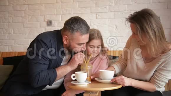 家人在咖啡馆休息家庭是母亲父亲和女儿人们坐在桌边他们快乐而微笑视频的预览图