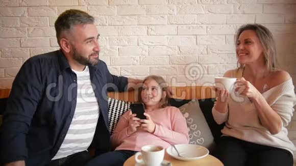 家人在咖啡馆休息家庭是母亲父亲和女儿人们坐在桌边他们快乐而微笑视频的预览图