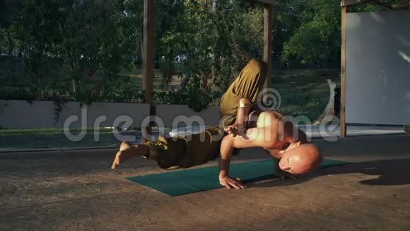清晨在城市公园光着身子的年轻赤脚男子在木助手上做瑜伽视频的预览图