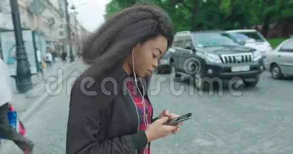 技术和人移动依赖迷人的年轻非洲女孩正穿过马路发短信浏览视频的预览图