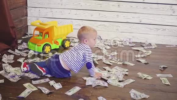 这个男孩在地板上玩玩具车那里有很多钱财富概念视频的预览图