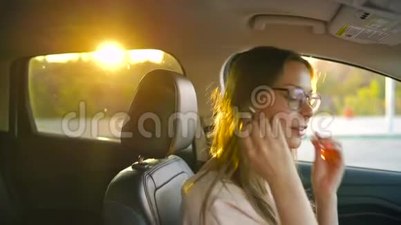戴着眼镜的漂亮女孩把无线耳机插到耳朵里系好安全带就要开车走了视频的预览图