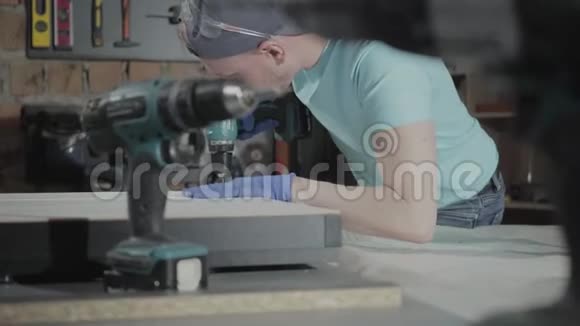 肖像年轻总工程师专注于在一个小作坊的背景上用工具钻孔视频的预览图
