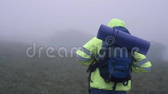 一位身穿信号背心连帽衫背着背包的游客的肖像是一幅雾中的群山后景慢影视频的预览图