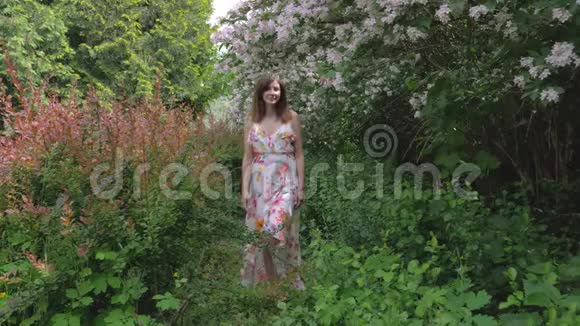 年轻美女走在鲜花盛开的灌木丛旁视频的预览图
