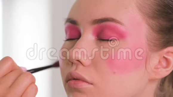 化妆师在摄影前将化妆产品应用在工作室的漂亮模特上视频的预览图