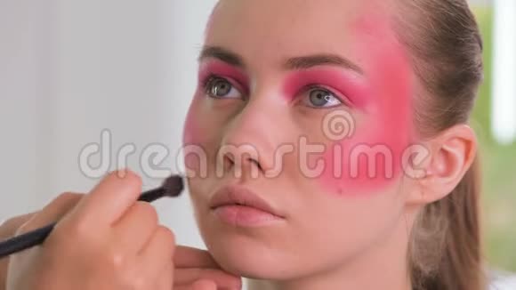 化妆师为年轻的金发女郎化妆刷做美丽的面部艺术视频的预览图