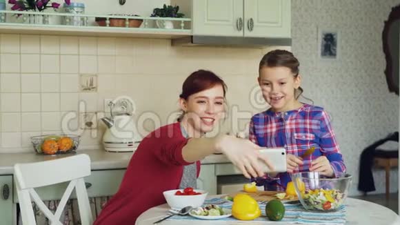 微笑的妈妈一起拍自拍照片和年轻可爱的女儿一起在厨房家做早餐家庭厨师视频的预览图