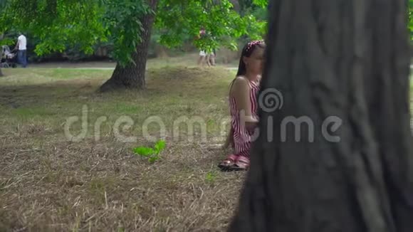 一个怀孕的女孩坐在公园的草地上一个穿着条纹白红色连衣裙的长发女孩正在看书视频的预览图