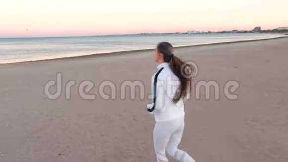 秋日日出时年轻女子正在海边的沙滩上慢跑侧观视频的预览图