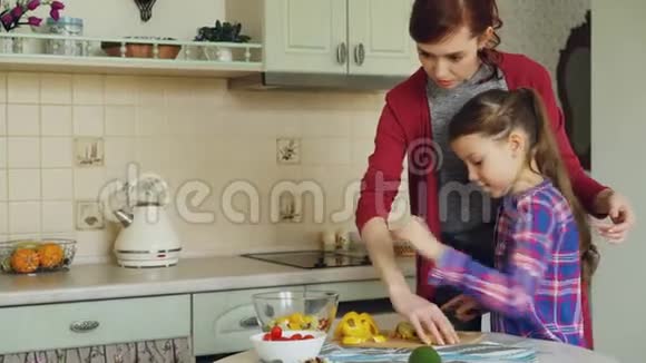 年轻漂亮的母亲教她可爱的女儿正确地切蔬菜小女孩和爱的妈妈一起做饭视频的预览图