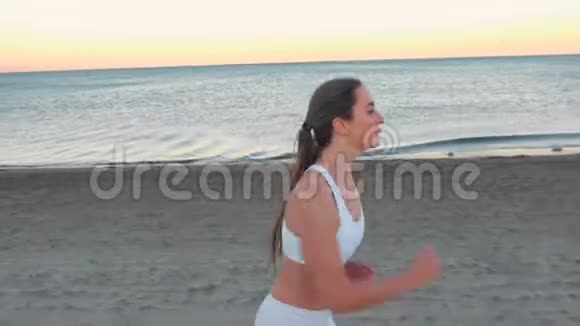 秋日日出时年轻女子正在海边的沙滩上慢跑侧观视频的预览图