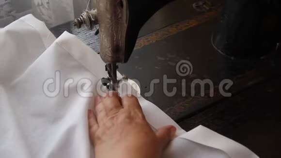 一位老妇人的手在一台旧的手工缝纫机上涂鸦白布双边面料封边处理视频的预览图