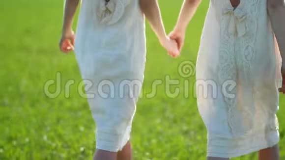 在一个阳光明媚的日子里两个穿着白色亚麻衣服的女孩沿着农村的一片绿色草地散步身体部位视频的预览图