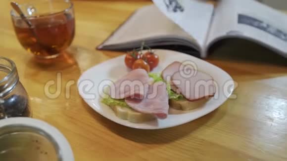 在厨房吃早餐时看杂志含西红柿的火腿三明治视频的预览图