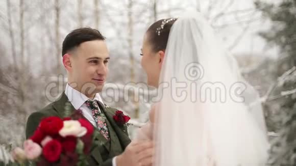 新婚的新郎和新娘在白雪皑皑的常绿林中拥抱亲吻和抚摸视频的预览图