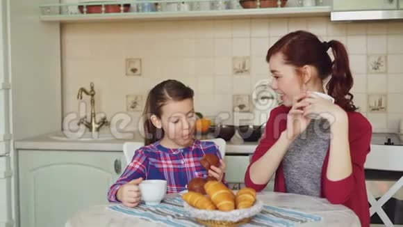 快乐的母亲和可爱的女儿吃早餐在现代厨房里吃松饼在家里聊天家庭食物家视频的预览图