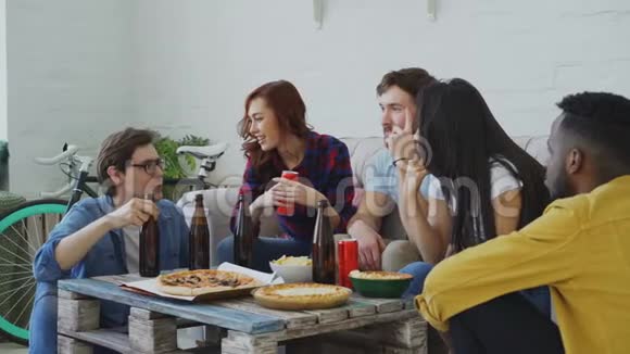 多种族的年轻快乐的朋友在喝啤酒和吃东西的时候坐在一起聊天视频的预览图