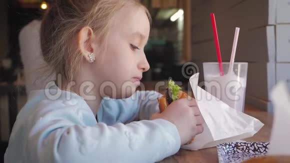 美丽快乐饥饿的女婴在咖啡馆里吃美味的不健康汉堡快餐概念慢动作录像视频的预览图