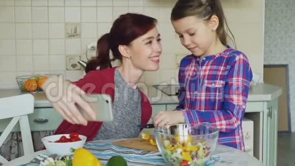 微笑的妈妈一起拍自拍照片和年轻可爱的女儿一起在厨房家做早餐家庭厨师视频的预览图