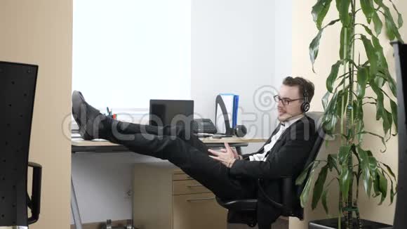 穿西装的年轻人坐在办公室的椅子上用耳机60fps说话视频的预览图