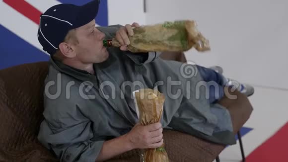 穿着帽子和外套的白人成年人躺在沙发上吃面包和饮料视频的预览图