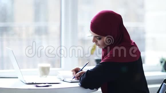迷人的穆斯林女孩正在她的笔记本上写一些东西然后开始在笔记本电脑键盘上打字印度支视频的预览图