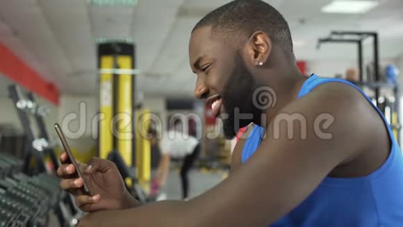 健身俱乐部成功的微笑运动员在智能手机上滚动照片视频的预览图
