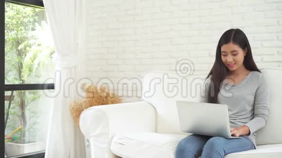 美丽的亚洲女人享受时光坐在窗前的现代沙发上在客厅里放松微笑着视频的预览图
