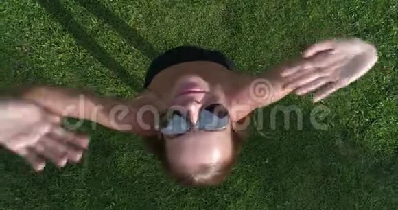 无人驾驶飞机从她脸上摘下太阳镜时站在草地上的女性的鸟瞰图视频的预览图