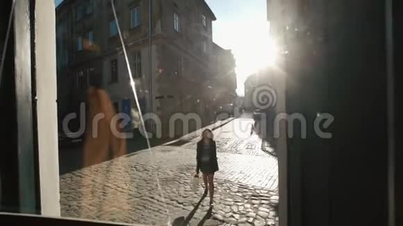 美丽的瘦小女孩正走进黑暗的咖啡馆透过门玻璃观看沿着阳光明媚的街道散步视频的预览图