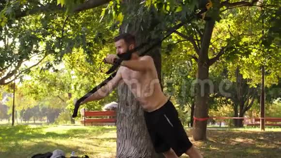 长胡子的年轻运动员在树旁用健身圈进行俯卧撑锻炼4K慢莫特写镜头视频的预览图