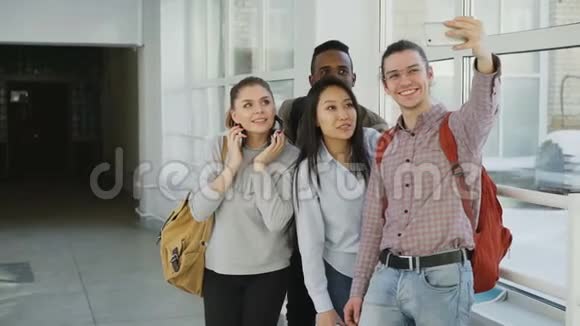一群多民族的学生在大学走廊里站在智能手机相机上自拍偷鸡仔视频的预览图