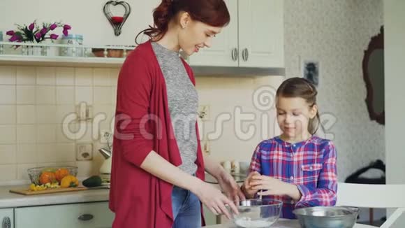 一个快乐的小女孩在厨房里帮妈妈把鸡蛋切成碗把面团搅拌成饼干家庭食物视频的预览图