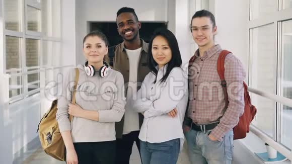 站在宽敞的白色走廊上的四个微笑积极吸引多民族男女学生的画像视频的预览图