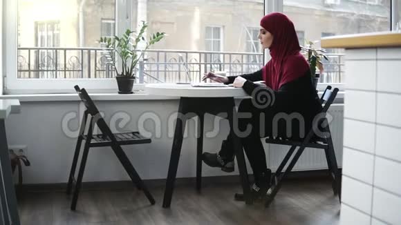 美丽的穆斯林女孩戴着头巾正在她的笔记本电脑上寻找一些东西并写下一些东西视频的预览图