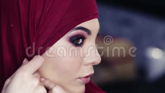 一个长着榛子眼睛头上戴着紫色头巾的美丽女孩正在调整她传统的阿拉伯头视频的预览图