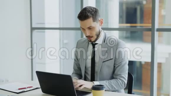 年轻的商人用手提电脑接收良好的信息并变得非常兴奋和快乐坐在现代办公室视频的预览图