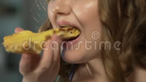 丰满的女孩咬着油腻的比萨饼片仔细咀嚼暴饮暴食的快餐视频的预览图