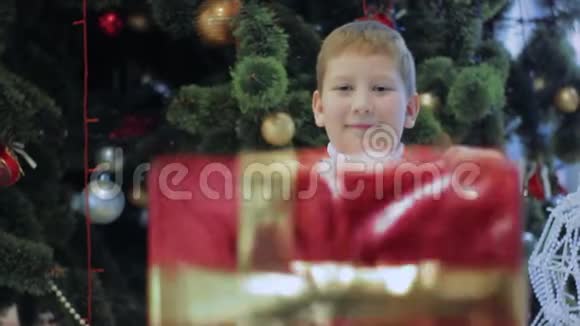 快乐的微笑男孩展示了红色新年礼物小孩站在圣诞树下视频的预览图