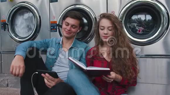 一对美丽的情侣在洗衣间听着电话里的音乐看书看视频英俊的年轻人视频的预览图
