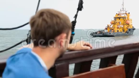男游客乘游艇驶过为油井服务的驳船视频的预览图