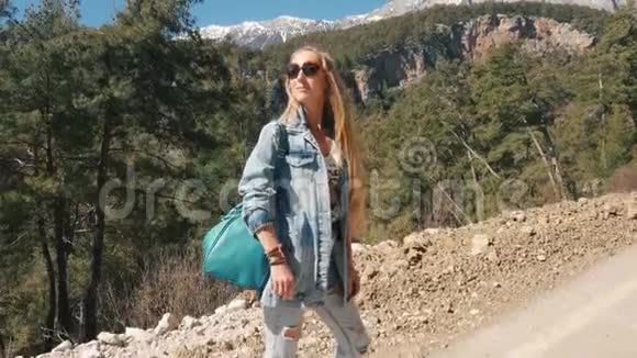 漂亮的年轻女士穿着牛仔裤拿着大手提包在户外搭便车阳光明媚视频的预览图