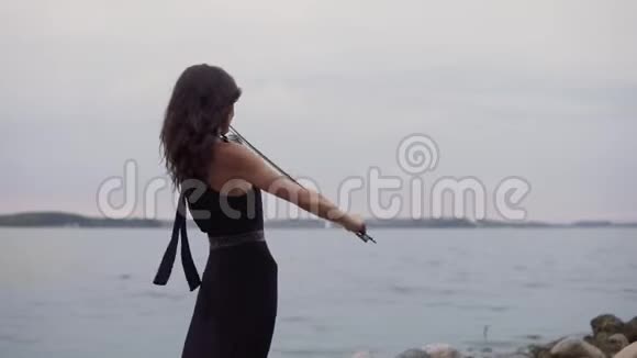 穿黑色连衣裙的漂亮女孩在海上拉小提琴4k的艺术概念视频的预览图