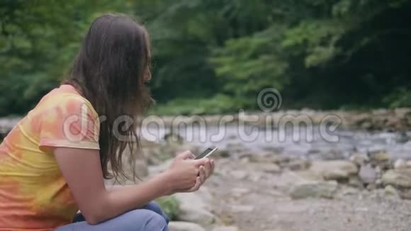 在河边休息的时候年轻女子在浏览手机视频的预览图