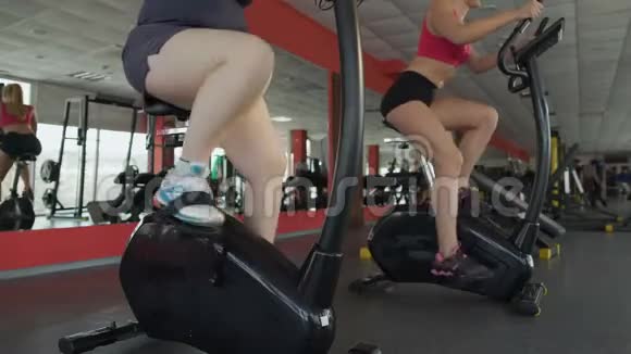 丰满苗条的女人在健身房骑着固定自行车的腿运动视频的预览图