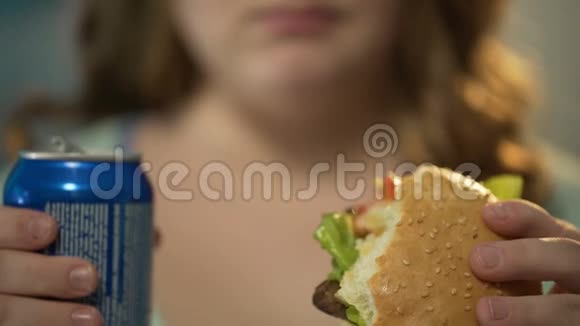 女孩吃高脂肪的汉堡喝罐头里的含糖苏打水吃过量的垃圾食品视频的预览图