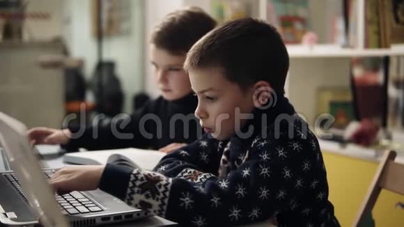 两个穿着温暖舒适毛衣的小男孩坐在笔记本电脑前的编程课上试图慢镜头视频的预览图