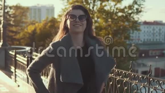 戴墨镜的迷人少女穿着外套穿过秋天的城市视频的预览图